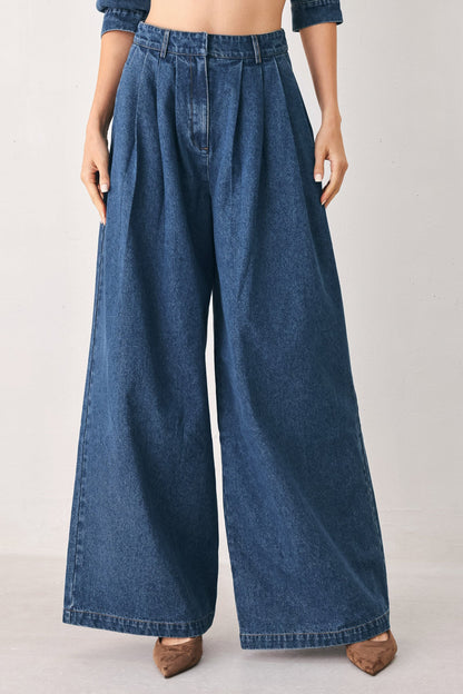 Medium indigo wide-leg denim pants styled with a matching denim jacket, light gray studio background.