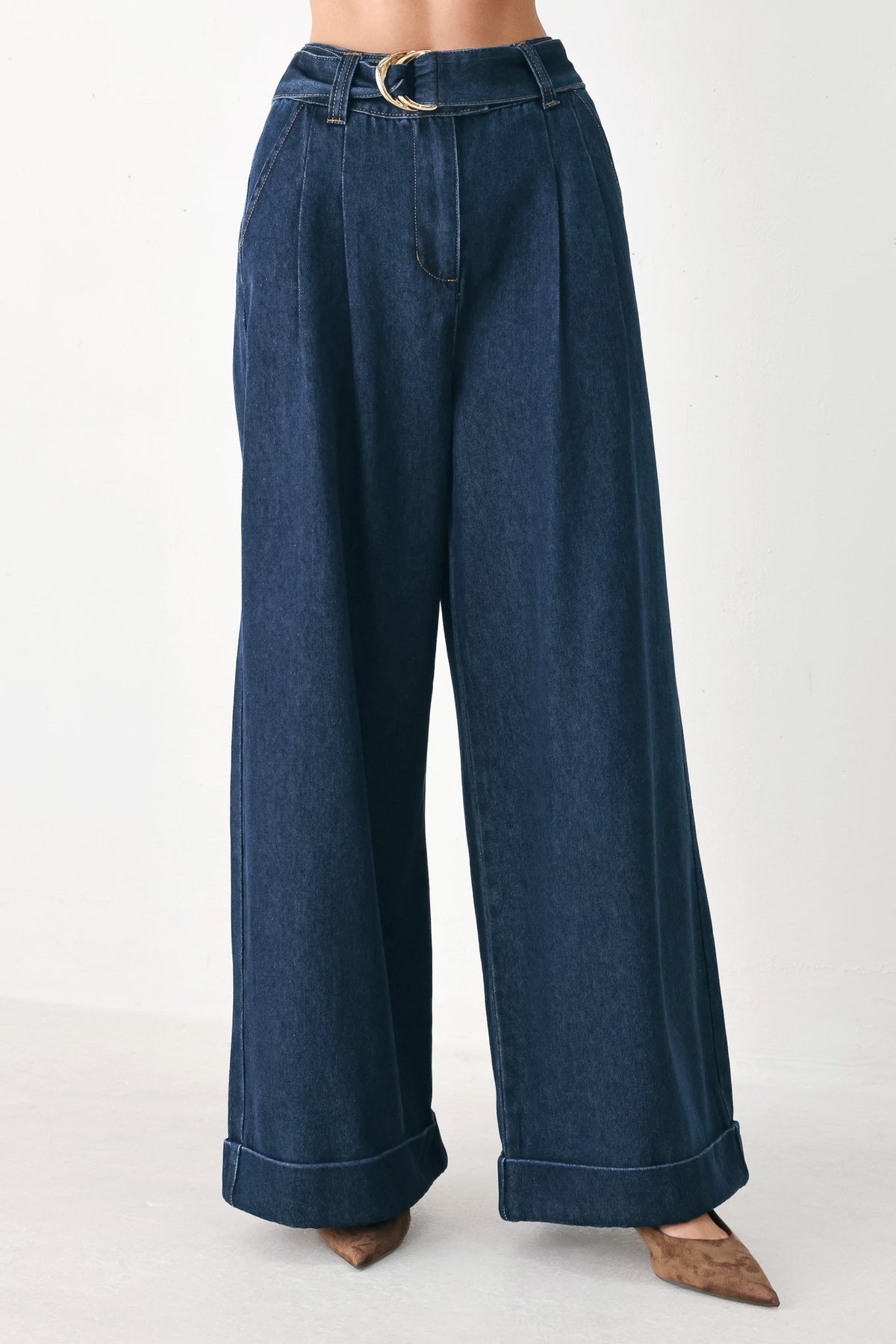 A person wearing dark blue wide-leg denim pants with a rolled cuff and a silver-tone belt buckle, shown from the waist down against a plain light background.