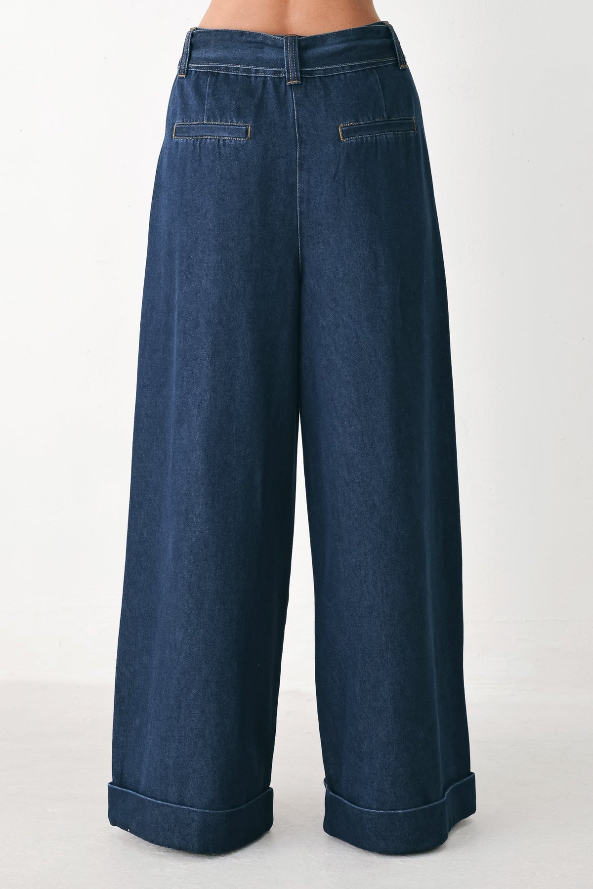 A pair of dark blue wide-leg denim pants shown from the back, featuring cuffed hems and back pockets, worn by a model against a plain white studio background.
