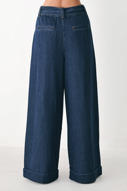 A pair of dark blue wide-leg denim pants shown from the back, featuring cuffed hems and back pockets, worn by a model against a plain white studio background.