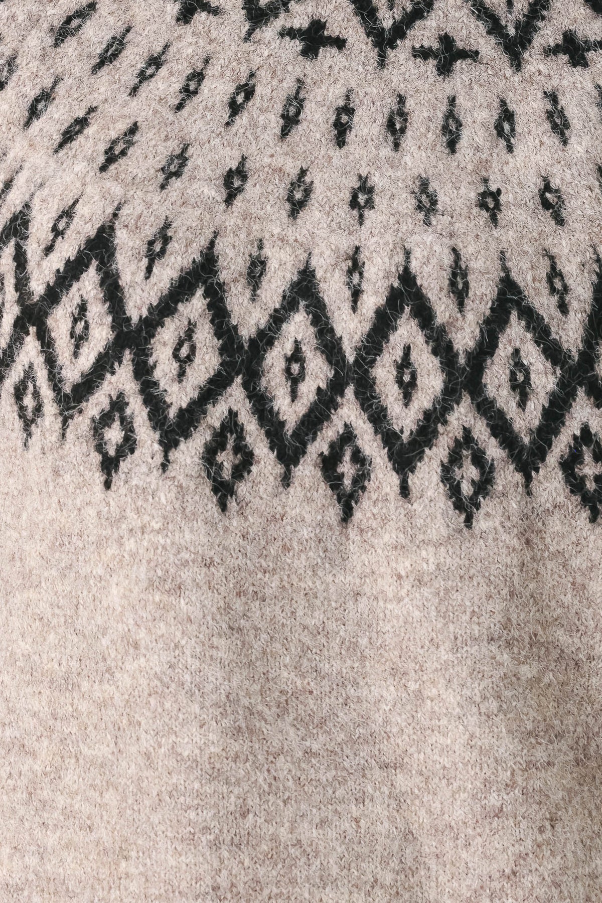 Close-up of a textured knit sweater showing a black geometric diamond pattern on a light beige heathered background.