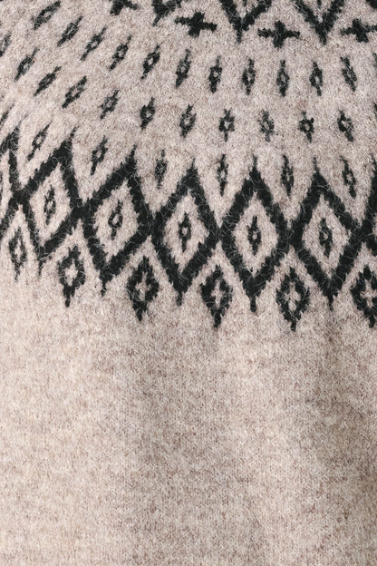 Close-up of a textured knit sweater showing a black geometric diamond pattern on a light beige heathered background.