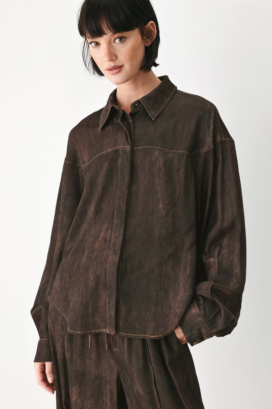 A model wearing a dark brown, washed-out faux-suede button-up shirt with matching dark brown trousers, photographed against a clean white studio background.