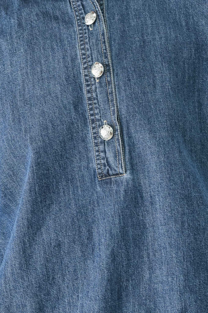 Close-up of a blue denim garment showing a buttoned placket with silver-toned buttons.