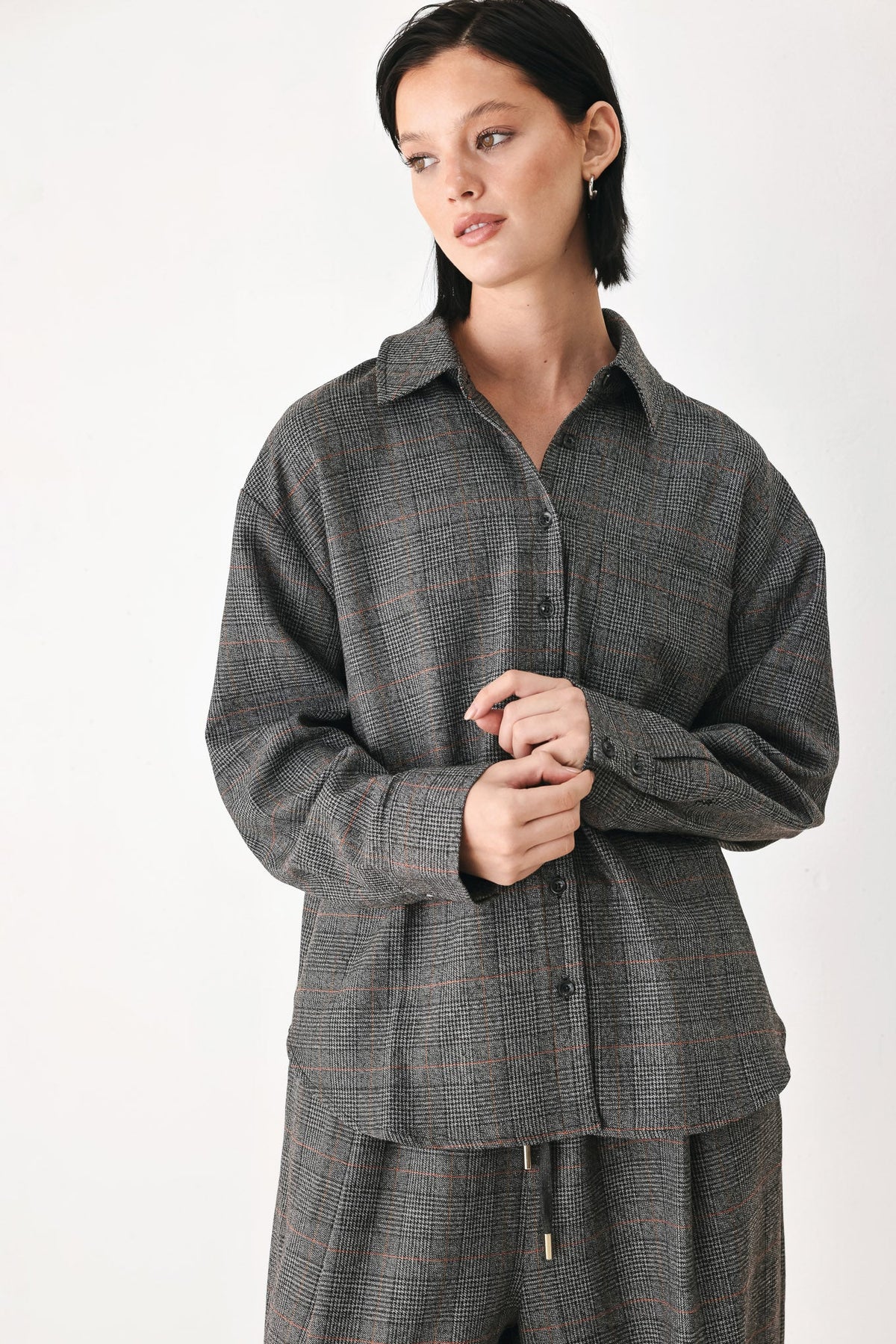 A model wearing a dark gray plaid button-up shirt and matching plaid trousers against a plain white studio background.