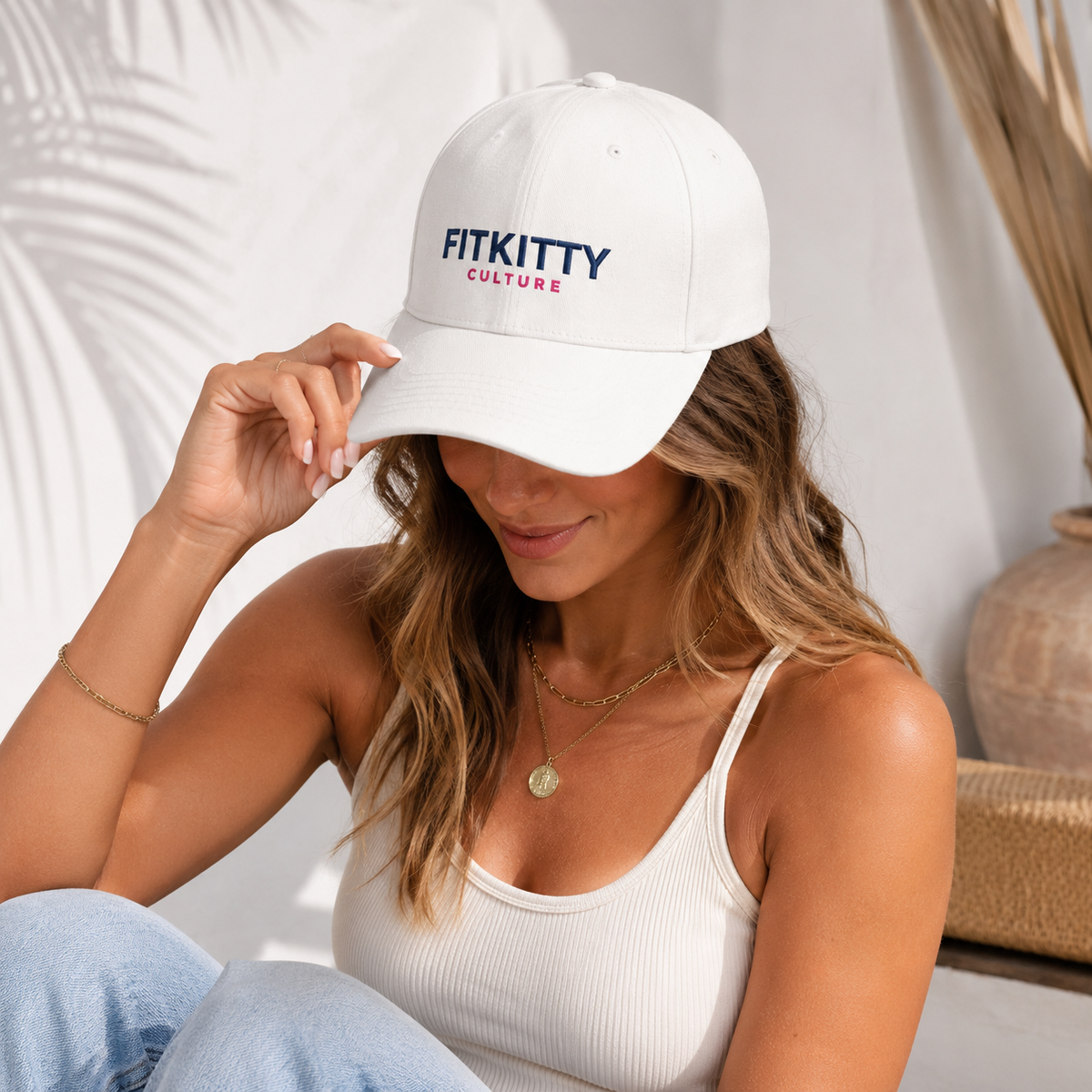 A woman wearing a white baseball cap with 'FITKITTY CULTURE' embroidered on the front, posing in a bright indoor setting.