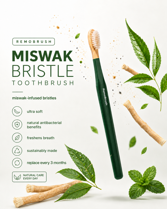 A Remobrush toothbrush with dark green handle and natural beige bristles, surrounded by mint leaves, tea tree branches, and floating droplets on a white background, with product text on the left.