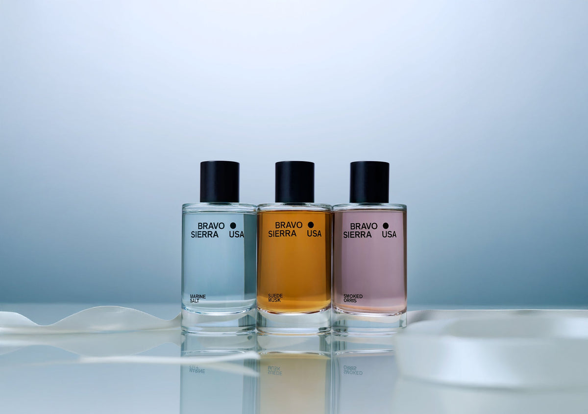 Three Bravo Sierra USA perfume bottles on a reflective surface with a light blue background