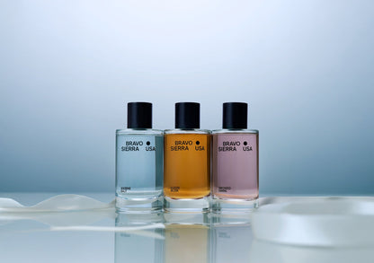 Three Bravo Sierra USA perfume bottles on a reflective surface with a light blue background