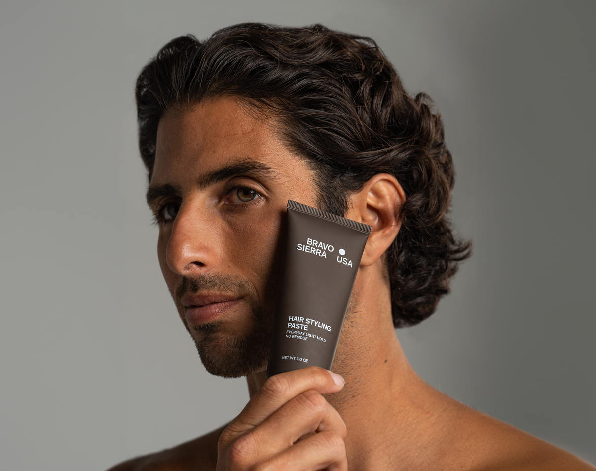 Man holding a bottle of hair styling paste against a gray background