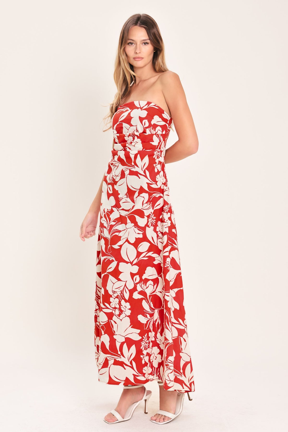 Woman wearing a red strapless dress with white floral pattern on a white background