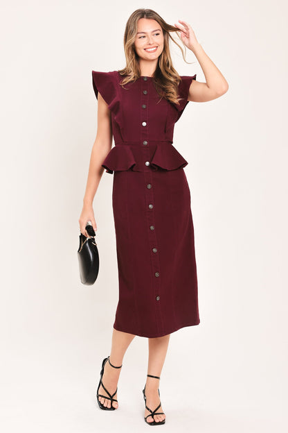 A woman models a sleeveless burgundy midi dress with ruffle details and a button-down front, paired with black strappy heels and holding a black clutch bag against a light beige studio background.