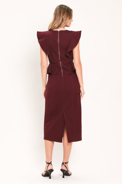 A woman viewed from the back wearing a sleeveless burgundy midi dress with dramatic ruffled shoulders, a front slit, and a central zipper. She is wearing black strappy heels against a plain white studio background.