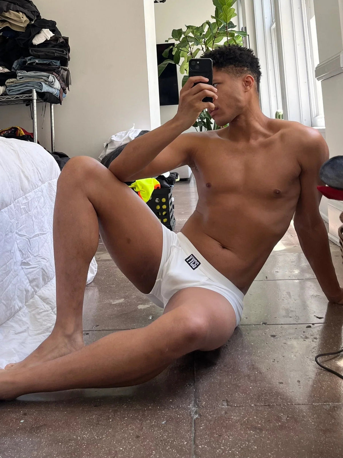 Man taking a mirror selfie wearing white underwear in a casual indoor setting.