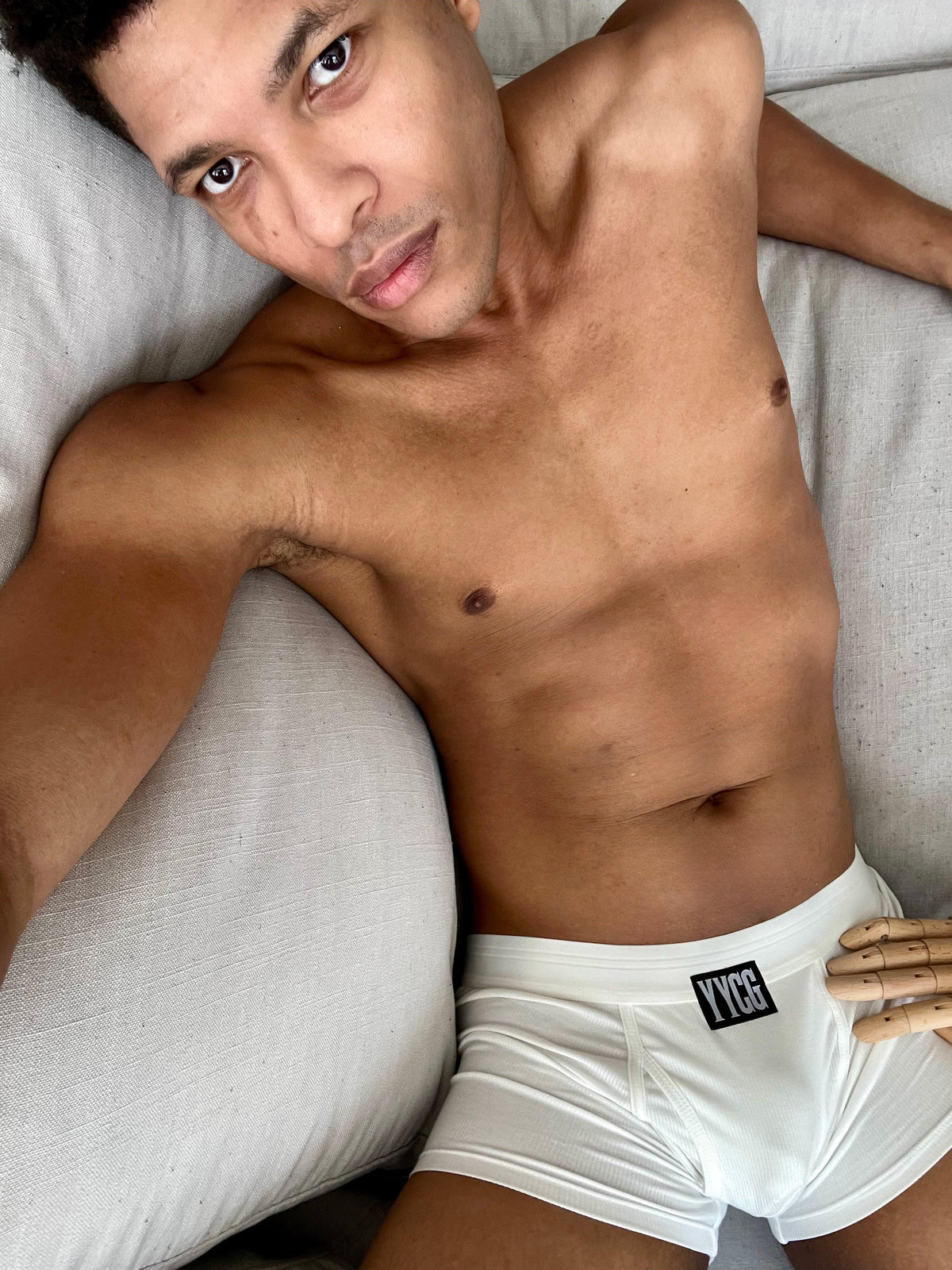 Man wearing white underwear with a brand logo, lying on a couch.