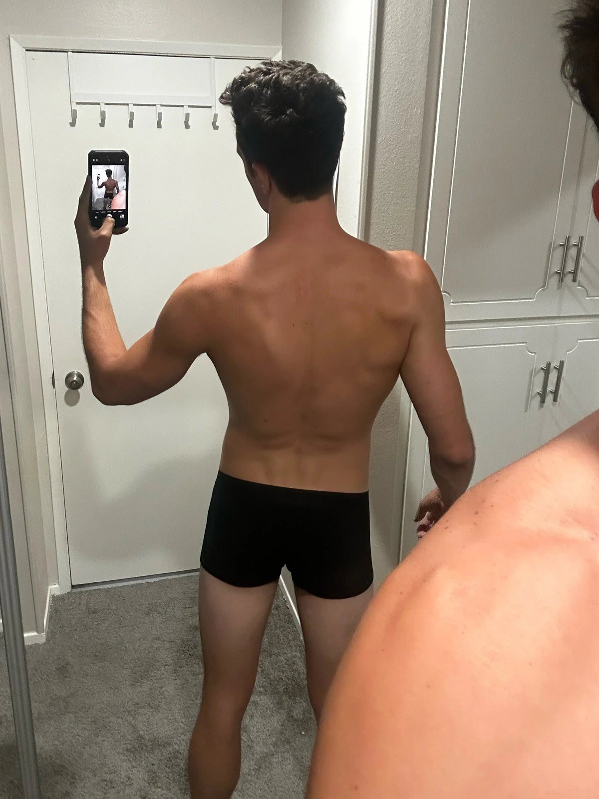 Person taking a mirror selfie wearing black underwear in a room.