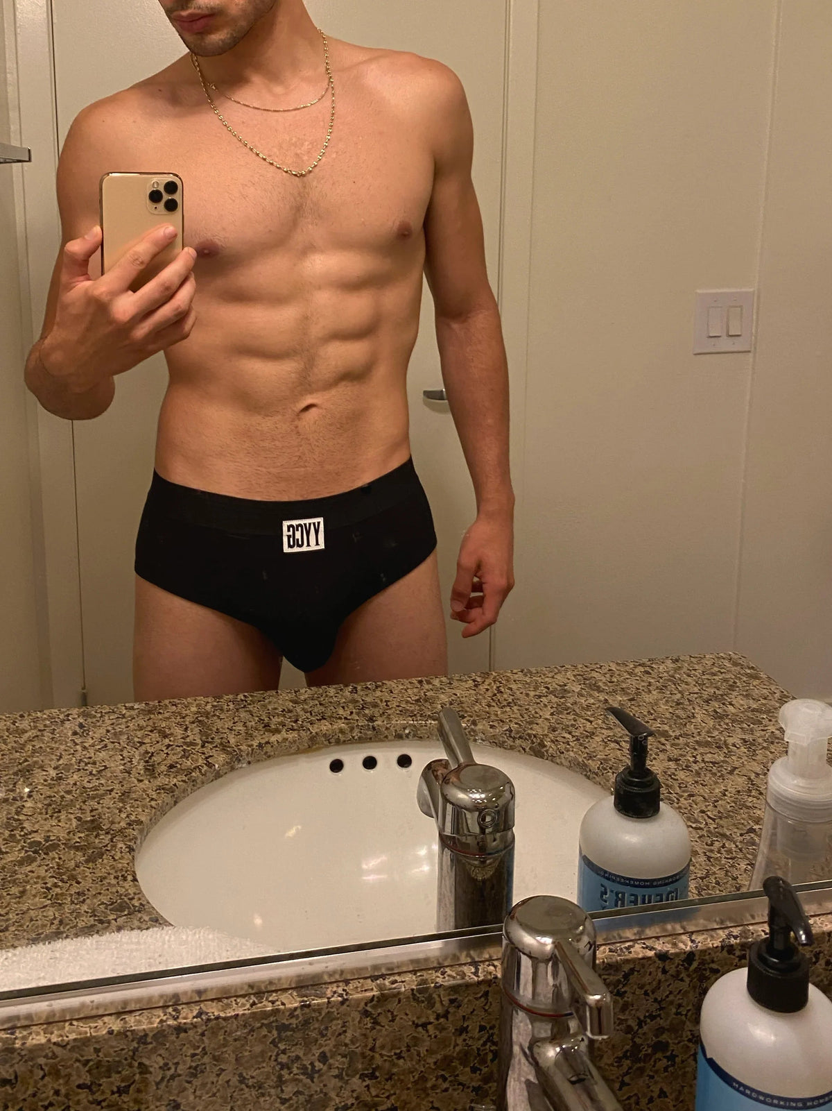 Man taking a mirror selfie wearing black underwear with visible branding in a bathroom.