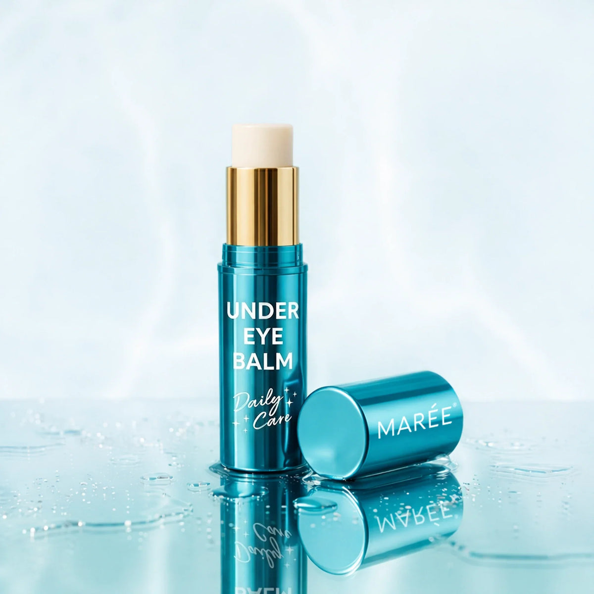 A teal under-eye balm stick with a gold collar and white balm tip stands upright on a glossy wet surface, with its cap placed beside it. The product is labeled 'UNDER EYE BALM Daily Care' and shows the brand 'MARÉE'.