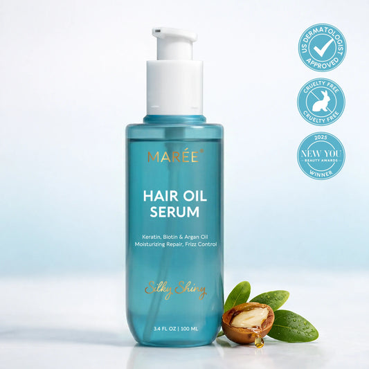 A bottle of MARÉE Hair Oil Serum in a translucent teal blue bottle with a white pump dispenser, shown on a light blue-white background with three circular certification badges on the right and a small nut and green leaves prop at the base.