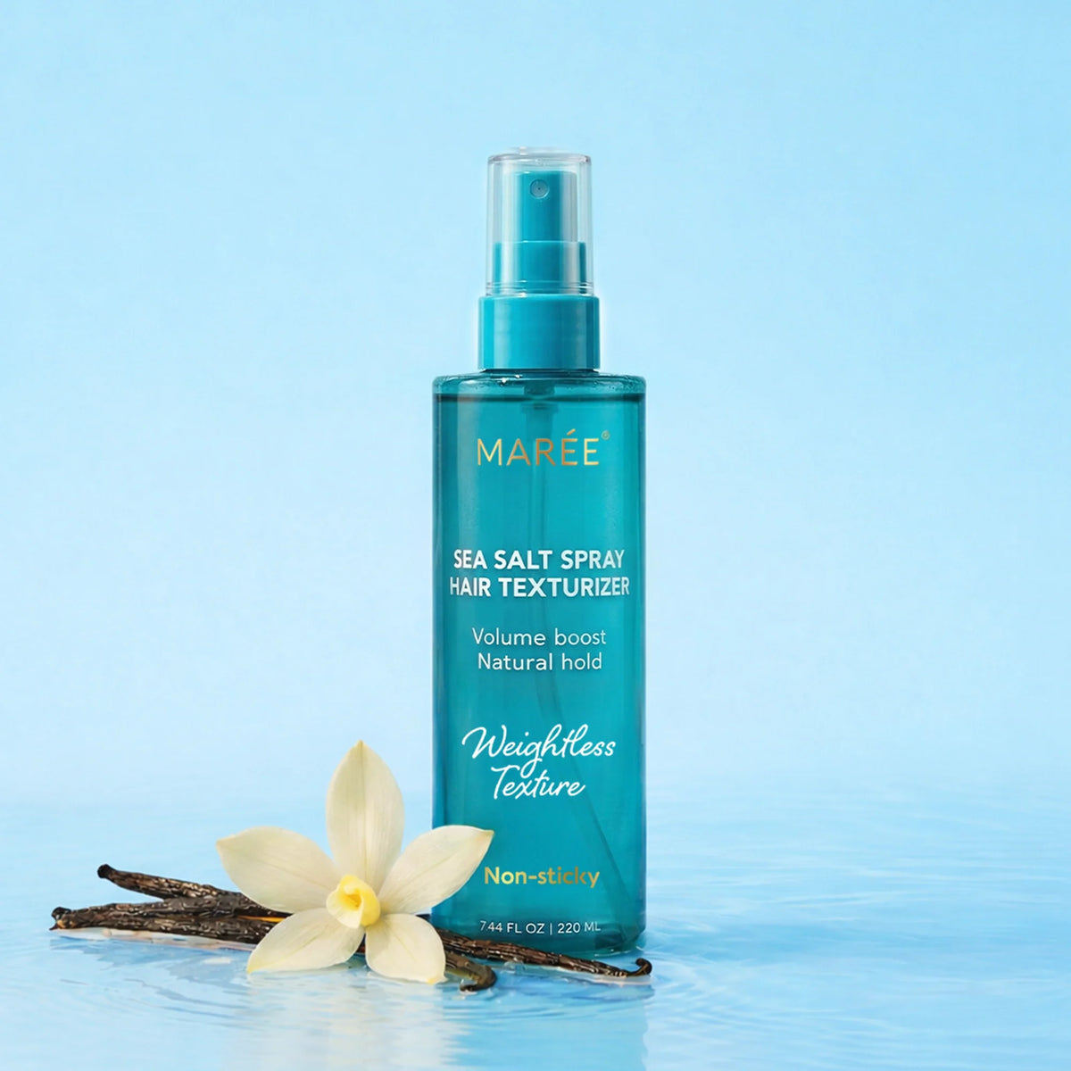 A bottle of MARÉE Sea Salt Spray Hair Texturizer stands on water with a white flower and vanilla beans beside it against a light blue background.