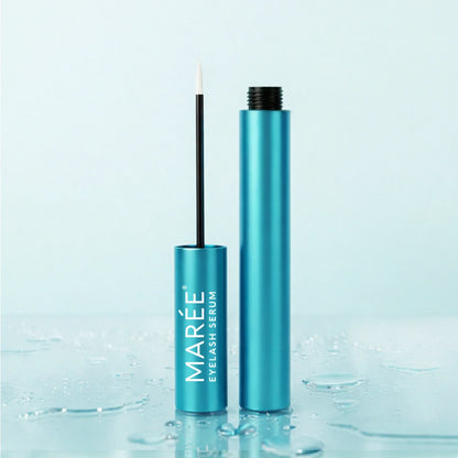 Marée eyelash serum in a metallic teal tube, shown with the applicator wand and open cap standing beside it on a glossy surface with water droplets against a pale blue background.