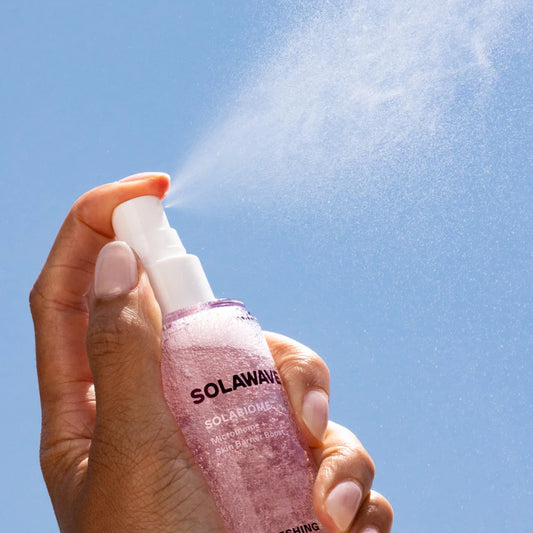 Hand holding a Solawave skincare product against a clear blue sky