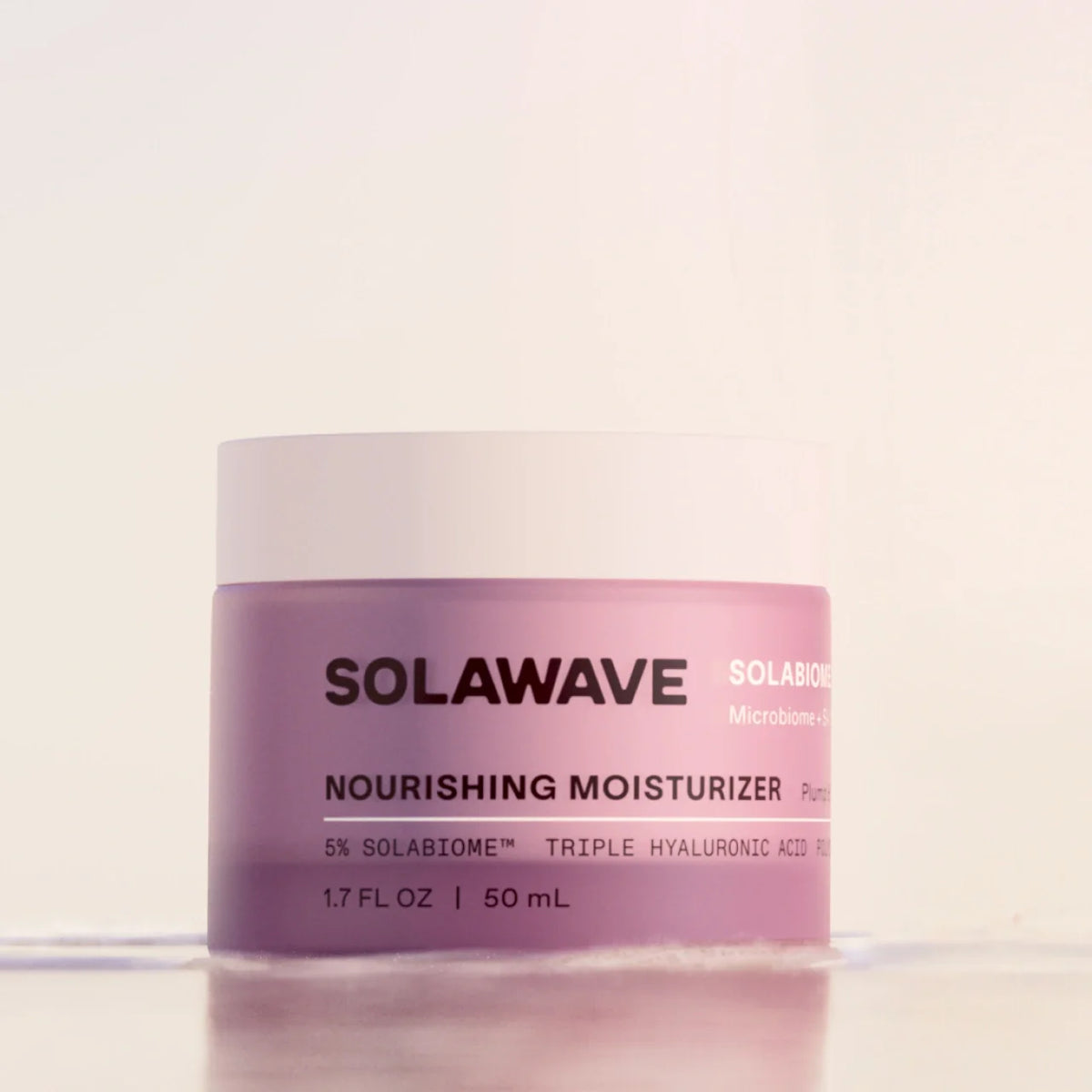 A jar of Solawave Nourishing Moisturizer with a light pink body and a white lid, set against a clean, off-white background.