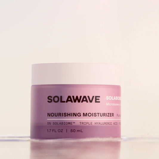 A jar of Solawave Nourishing Moisturizer with a light pink body and a white lid, set against a clean, off-white background.