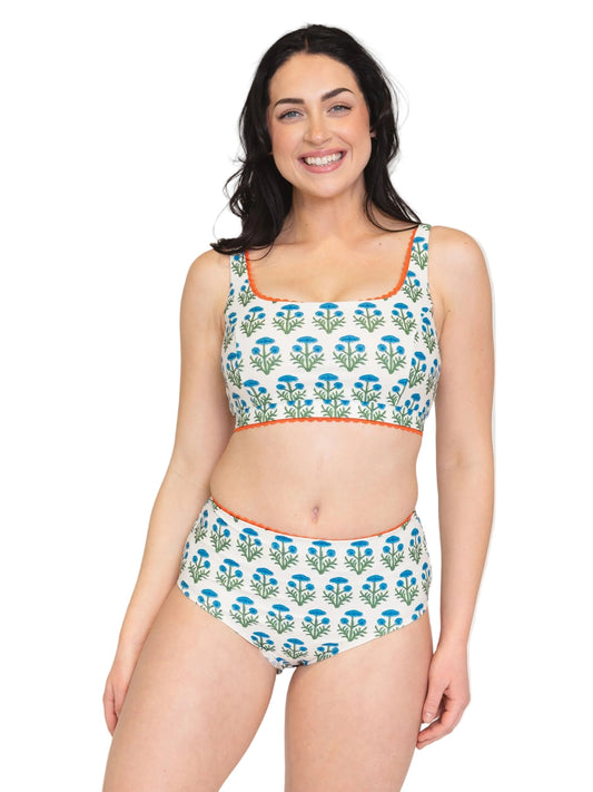A woman modeling a two-piece bikini set with a white background, blue and green floral pattern, and orange trim on a solid white studio background.