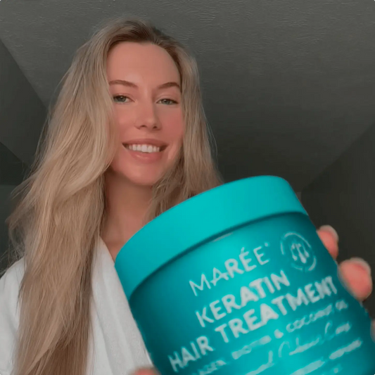 Woman holding a teal container of Maré Keratin Hair Treatment against a dark background