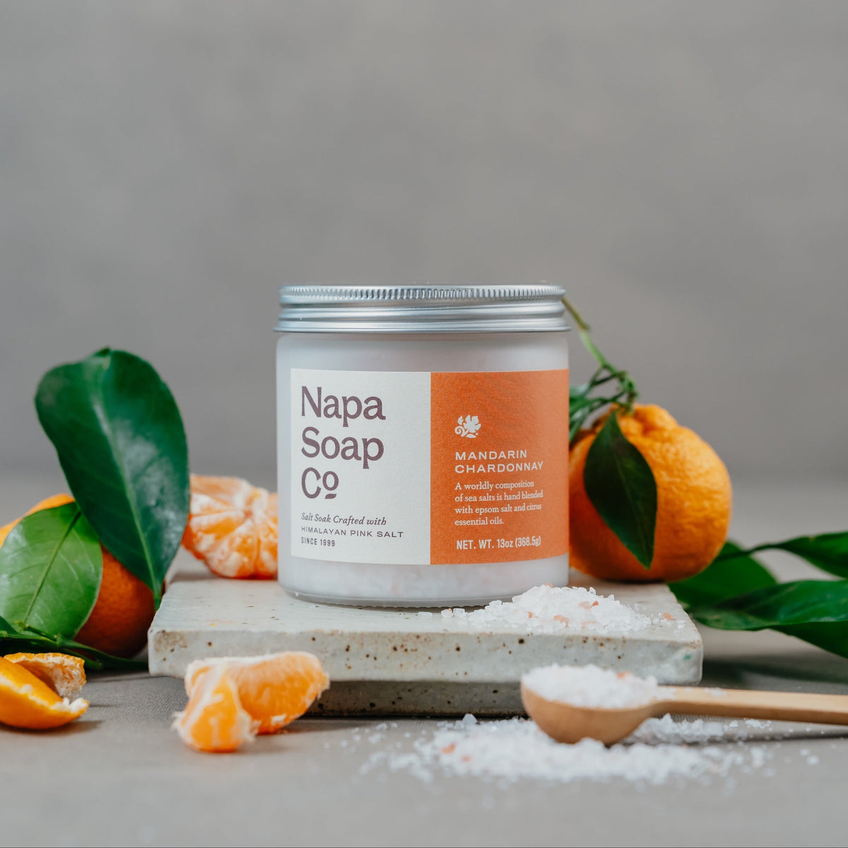 Mandarin Chardonnay bath salt soak with mandarin oranges and loose salt on a gray background