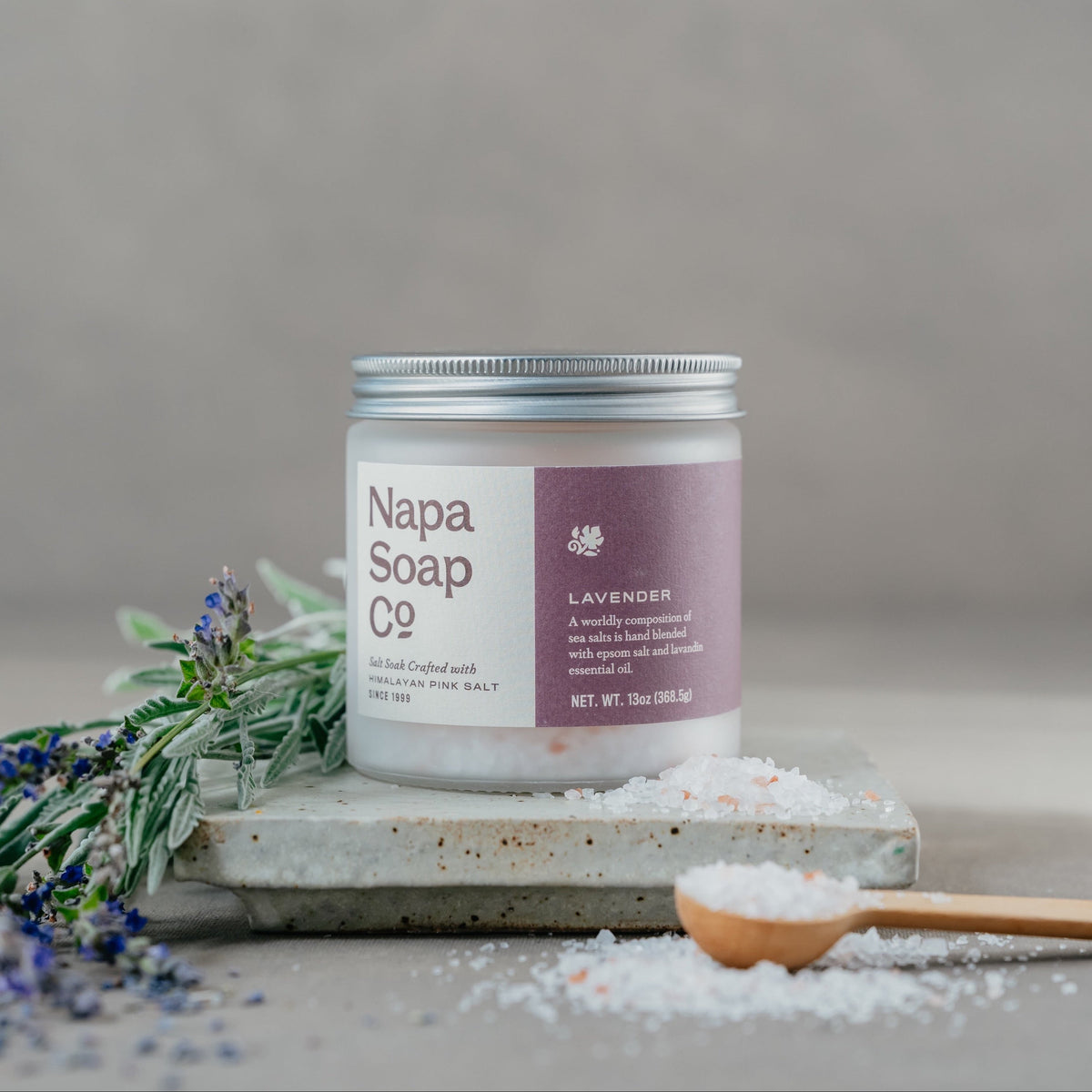 Lavender bath salt soak on a stone surface with lavender flowers and loose salt