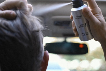 Person using a bottle of dry shampoo inside a car.