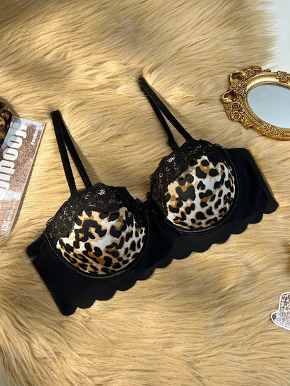 Black underwire bra with leopard print cups and black lace trim, laid flat on a beige faux fur surface with decorative props.