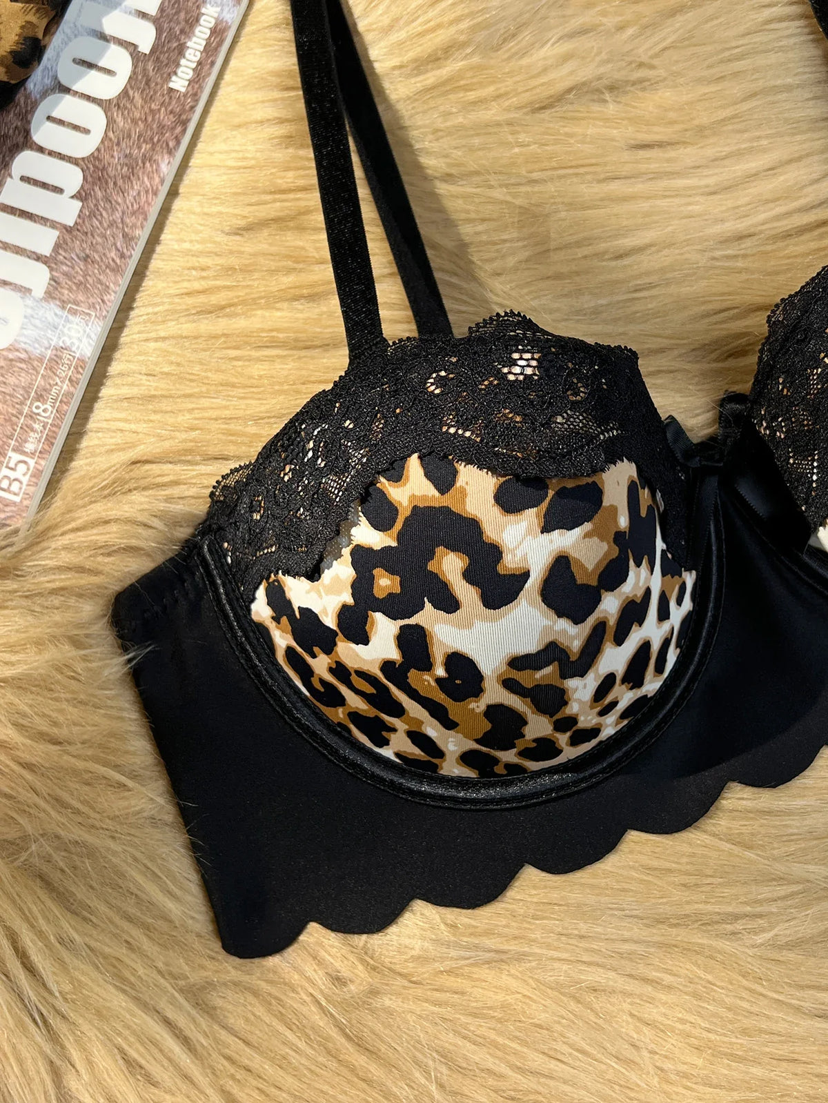 Black lace-trimmed bra with a leopard-print underwire cup, laid flat on a beige faux-fur surface.