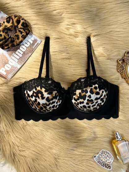 Black underwire bra with leopard print cups, laid flat on a beige faux fur background with decorative accessories around it.