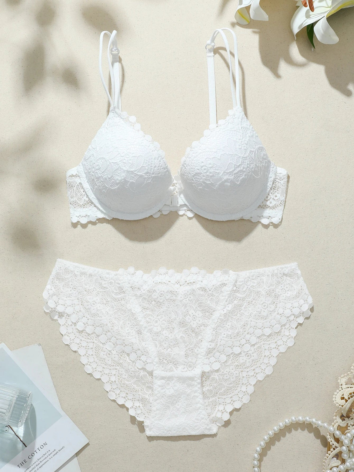 White lace bra and panties set on a beige surface with shadows.