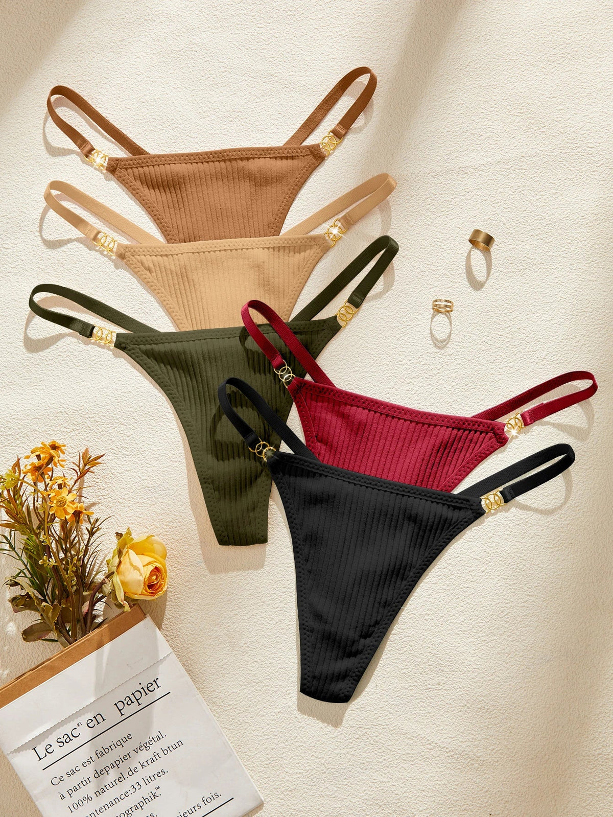 Four pairs of ribbed thongs in brown, beige, green, and red on a textured surface with a small plant and paper.