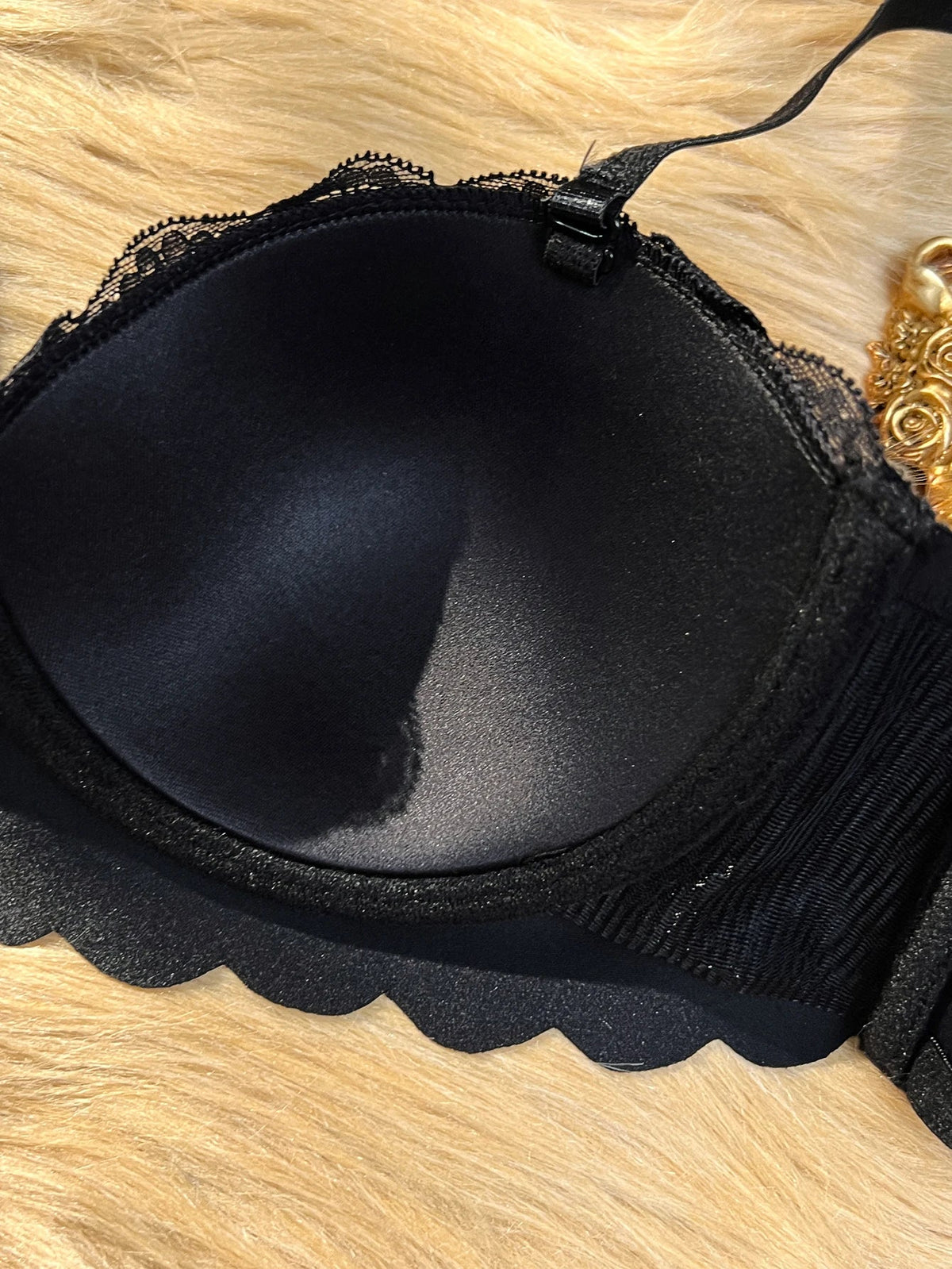 Black underwire bra with scalloped lace edges and a ribbed band, laid flat on a beige faux fur surface.