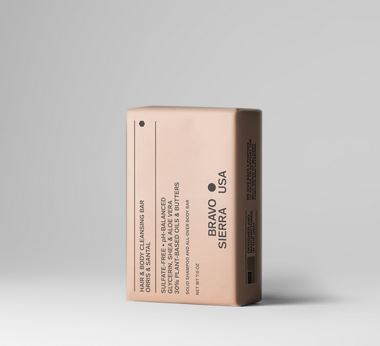 A single rectangular hair and body cleansing bar package standing upright on a clean light gray studio background. The package is a warm blush-beige color with black text reading BRAVO SIERRA USA and product details including coconut, shea, and argan oils.