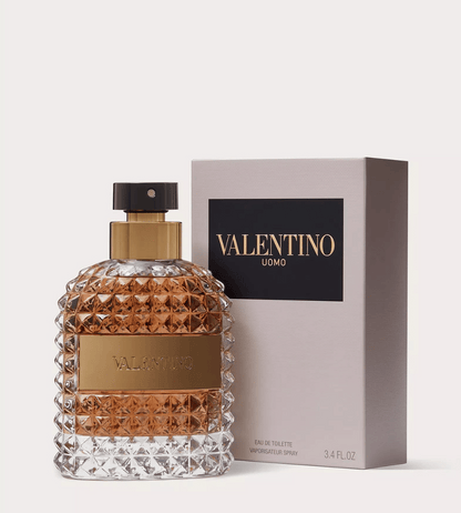 Valentino Uomo Eau de Toilette perfume bottle with a textured clear glass body and amber liquid, shown next to its light gray box with a black Valentino Uomo label.