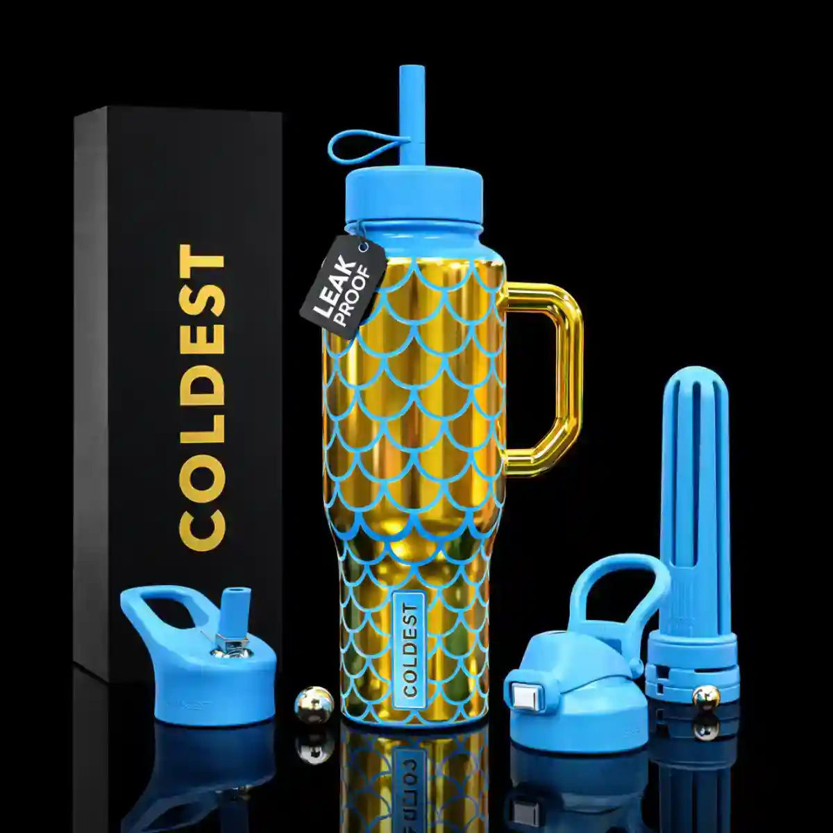 A blue and gold insulated tumbler with a handle, shown with its lid, straw, and separate blue components on a black reflective background. A black box with gold 'COLDEST' lettering stands beside it, and a small hang tag reads 'LEAK PROOF'.