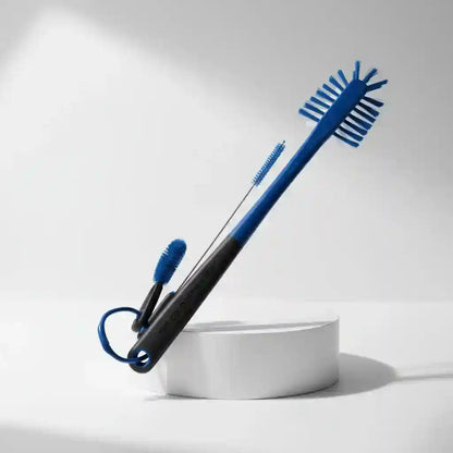 A blue and black cleaning brush set with two small blue bristle brushes, displayed on a white cylindrical pedestal against a clean white background.