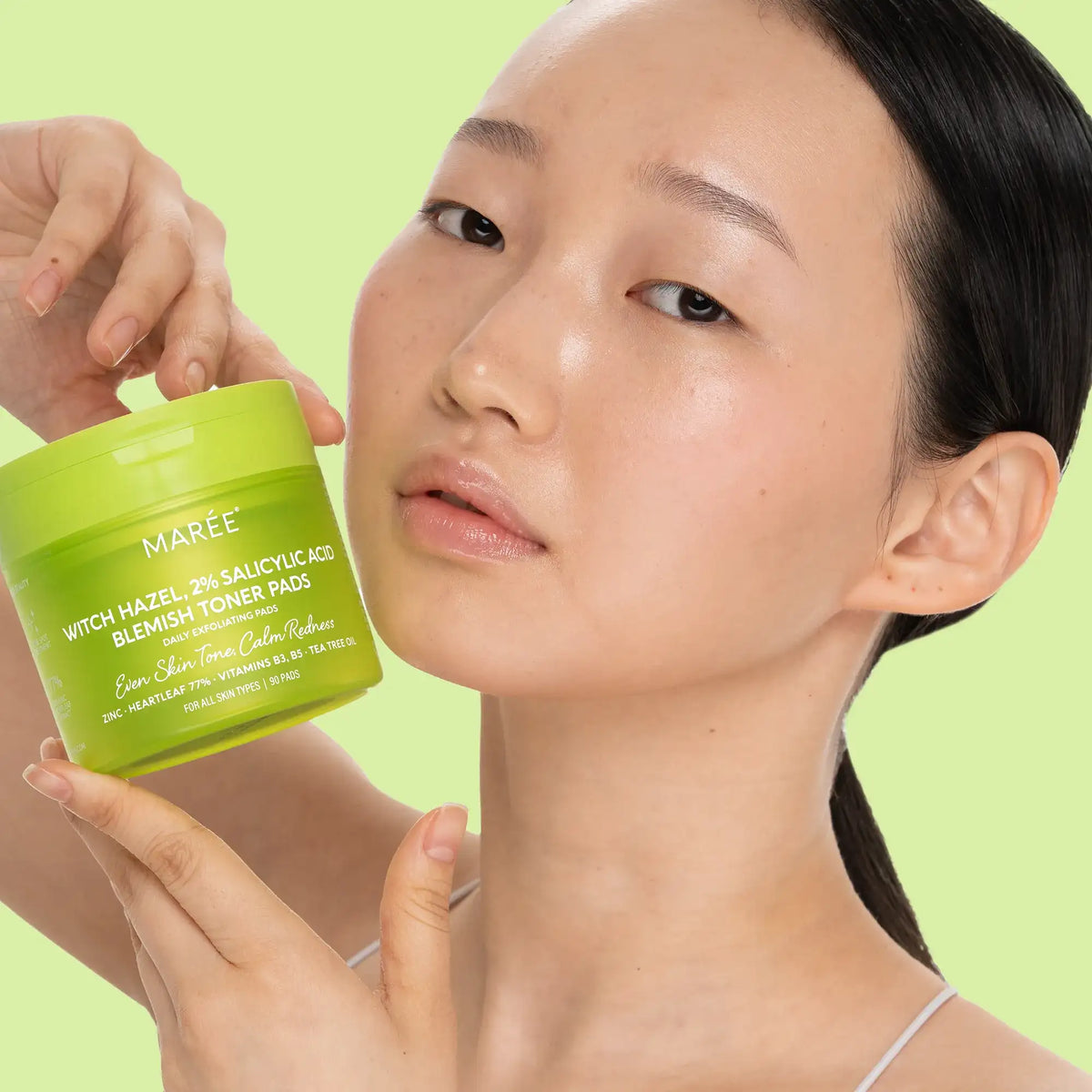 Woman holding a green jar of MAREE skincare product against a light green background
