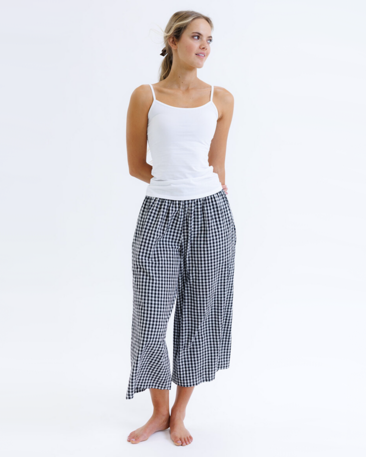 Woman wearing a white tank top and black and white checkered pants on a white background