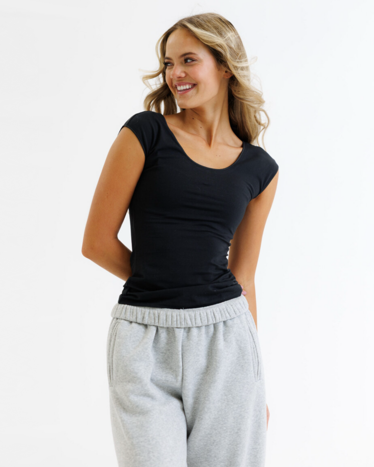 Woman wearing a black cap-sleeve top and gray sweatpants on a white background