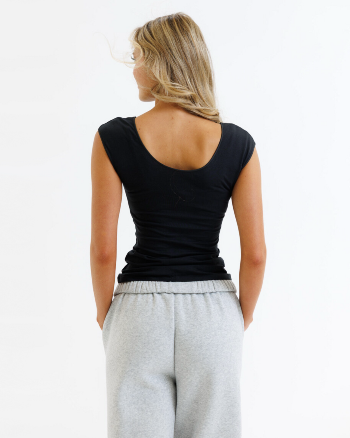 Woman wearing a black tank top and gray sweatpants on a white background