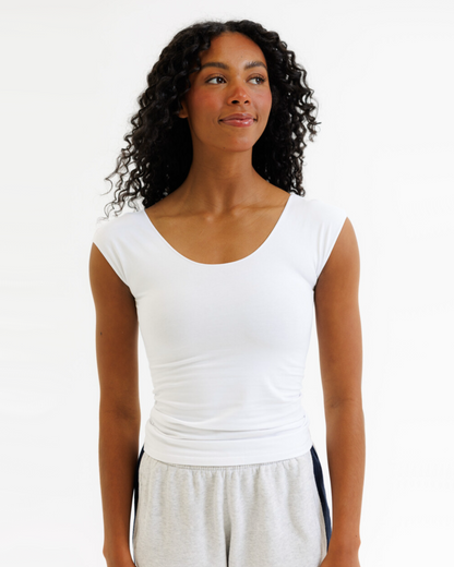 Woman wearing a white cap sleeve top and gray shorts on a white background