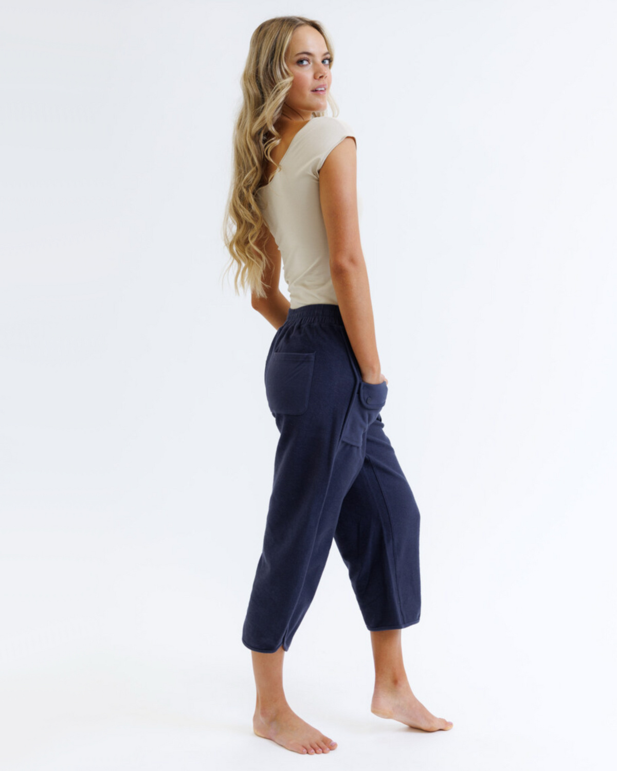 Woman wearing navy capri pants and a beige top on a white background