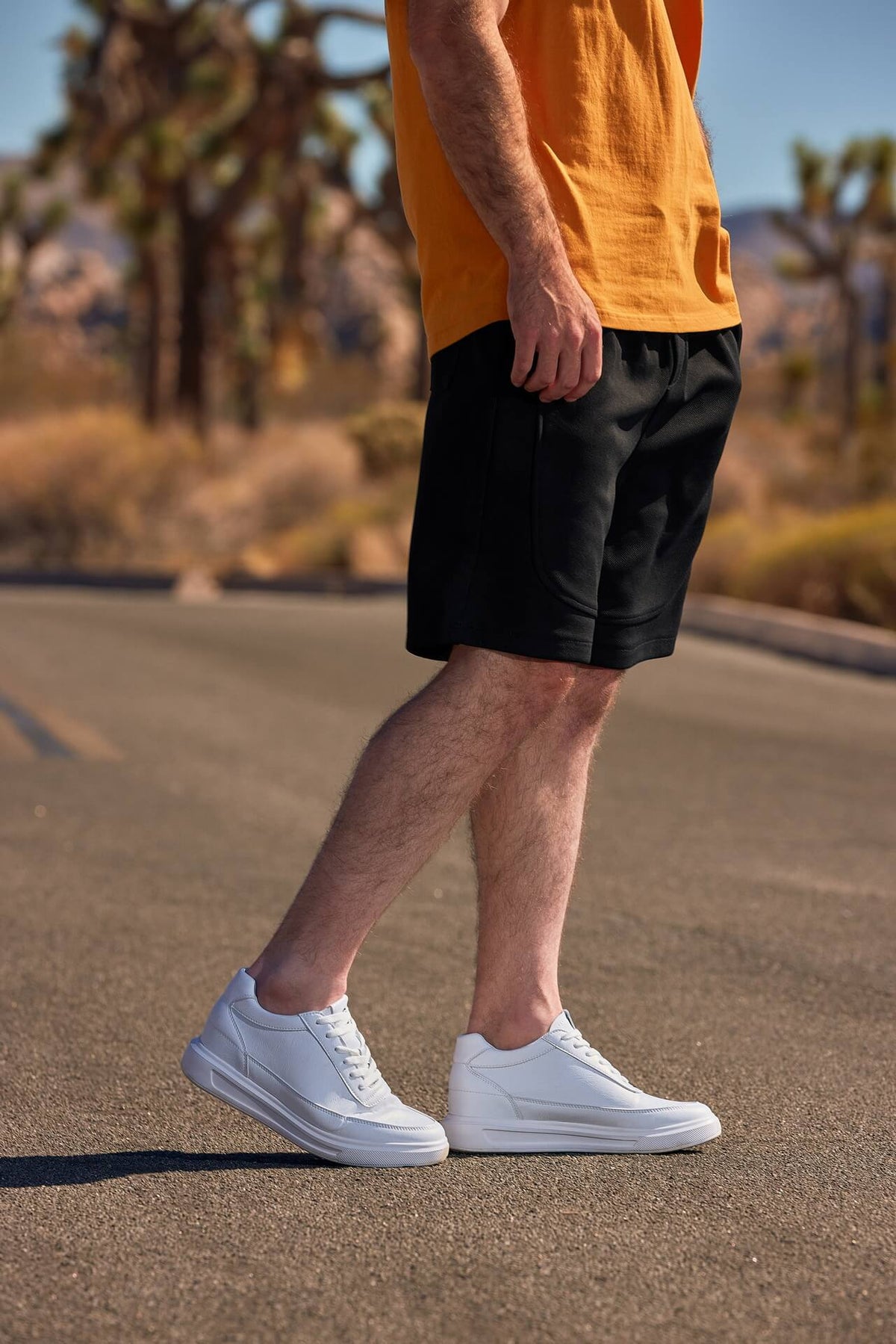 Person wearing black shorts and white sneakers on a road with desert landscape in the background